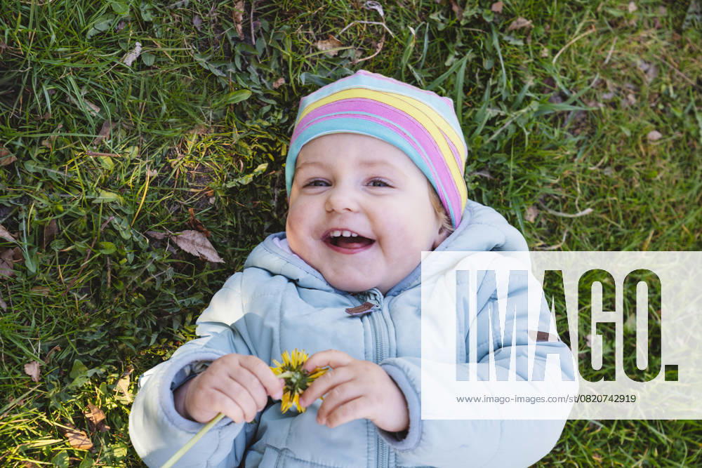 Smiling baby lying on grass outdoors wearing a colorful hat model released, Symbolfoto, IHF02200