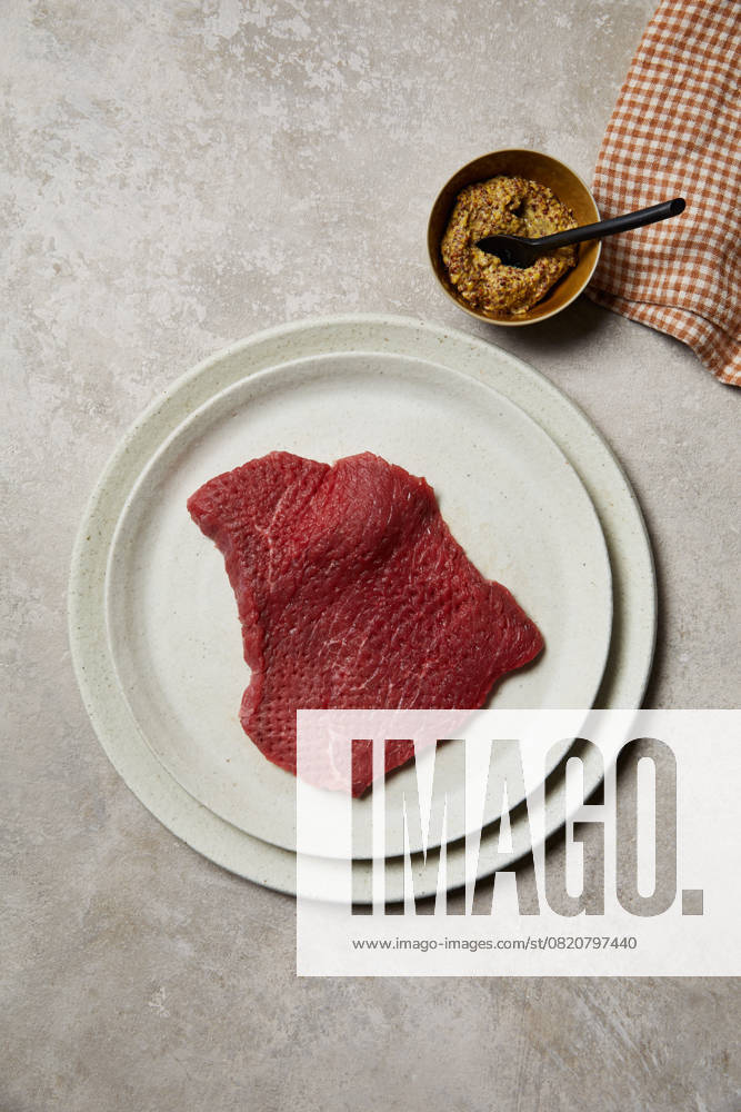 A fresh piece of beef steak displayed on a white ceramic plate, accompanied by grainy mustard in a small dish. Perfect for culinary and butcher themes, showcasing high-quality meat preparation. Model Released GeorgiaGold_ID28577_843651_042