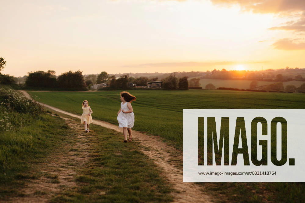 IMAGO Creative, Jahreszeit Sommer, Sommerferien Two young sisters running along a narrow country path at sunset. Corby, England, United Kingdom CR_JNDO250602-1745310-01 ,model released, Symbolfoto