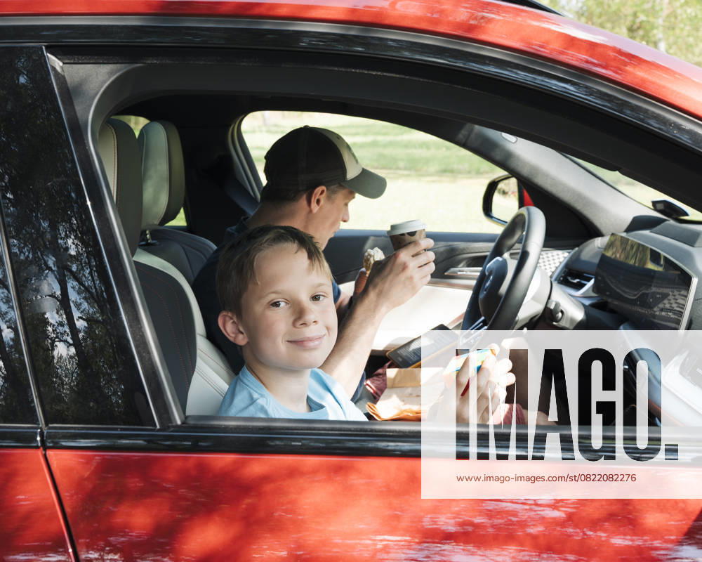 Father and son sat in the car together eating snacks and playing games Stockholm, Stockholm County, Sweden R_RABE250610-1759992-01