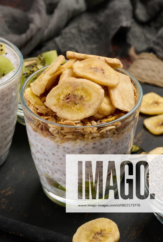 IMAGO Creative, Food, High Protein Frühstück Zwei Gläser mit Chiasamenpudding, eines mit gewürfelter Kiwi und das andere mit Granola und Bananenchips, stehen auf einer dunklen Fläche mit Zutaten Zwei Gläser mit Chiasamenpudding, eines mit gewürfelter Kiwi und das andere mit Granola und Bananenchips, stehen auf einer dunklen Fläche mit Zutaten (License=RF)