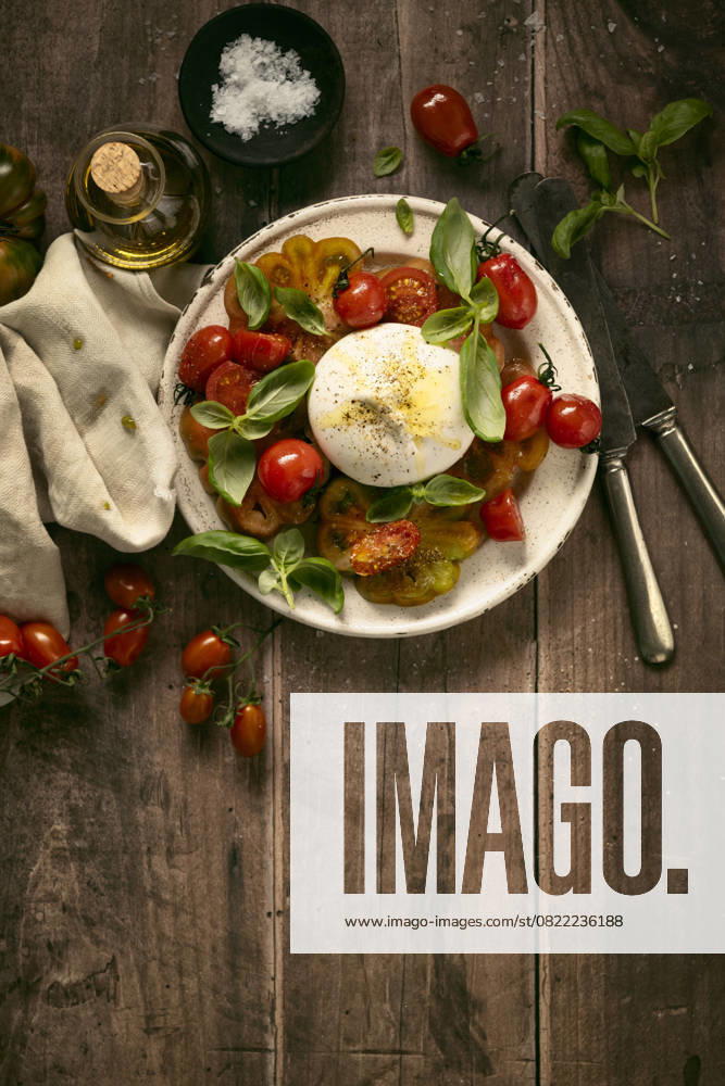 Directly above caprese salad, typical Italian food, representing the colours of the italian flag, with tomatoes, mozzarella and basil on wooden table directly above caprese salad, typical Italian food, representing the colours of the italian flag, with tomatoes, mozzarella and basil on wooden table