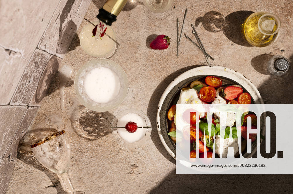 Directly above caprese salad with strawberries, in hard light, prosecco is being poured into a glass directly above caprese salad with strawberries, in hard light, prosecco is being poured into a glass