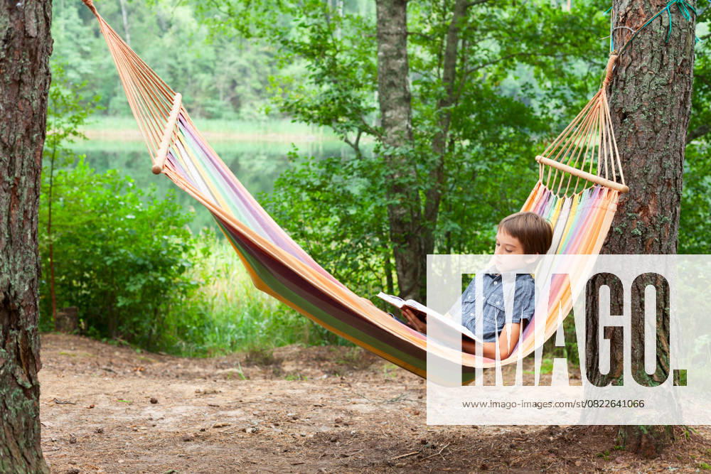 Kind liest Buch in der Hängematte Boy lying in hammock reading a book outdoors (License=RF) ,model released, Symbolfoto