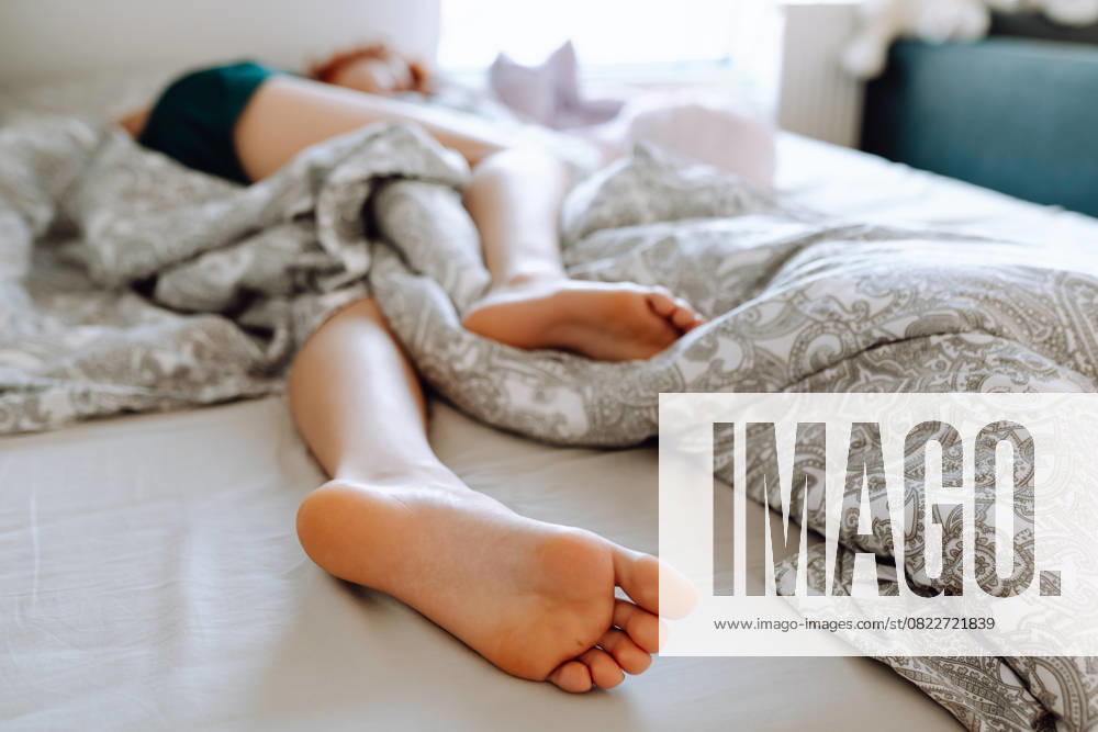Junge frau liegt auf dem bett mit nackten füßen, die von einer decke bedeckt sind. füsse nahaufnahme sleeping young woman lies on bed with bare feet uncovered by blanket. feet close up (License=RF) ,model released, Symbolfoto