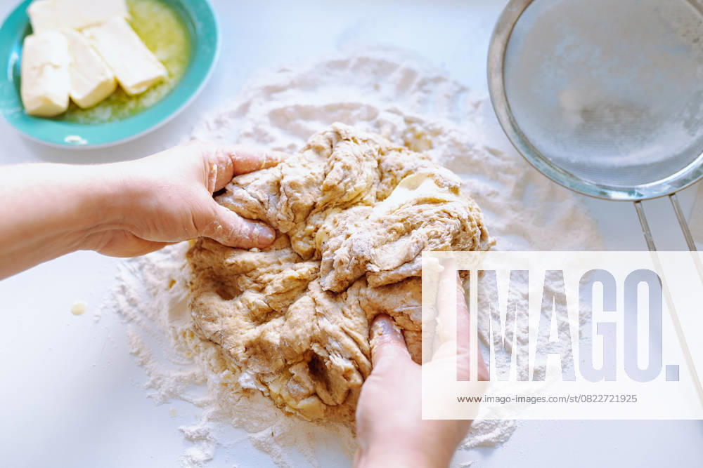 Weibliche Hände kneten Teig Women s hands, in flour, knead yeast dough for pastries, on kitchen table, sprinkled with flour, nearby there is butter on plates, colander for sifting flour (License=RF)