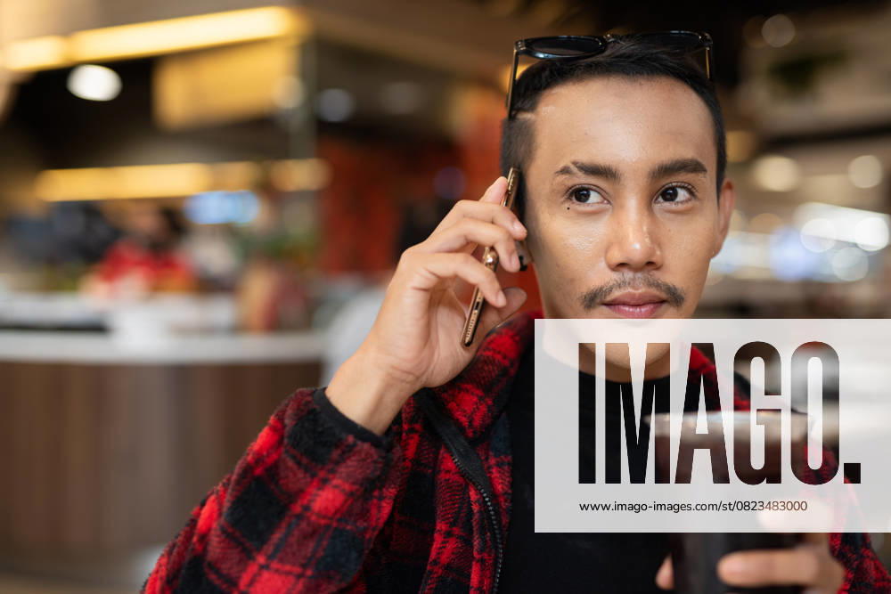 IMAGO Creative, Food, Trend, Iced Coffee Porträt eines jungen asiatischen schwulen Mannes mit nichtbinärem Geschlecht, der mit dem Telefon telefoniert Porträt eines jungen asiatischen schwulen Mannes mit nichtbinärem Geschlecht, der mit dem Telefon telefoniert (License=RF) ,model released, Symbolfoto