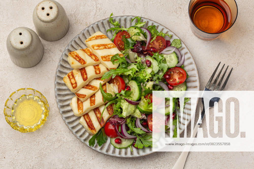 Gebratener Halloumi-Käse mit frischem Gemüsesalat auf Keramikteller, Draufsicht, heller Hintergrund fried halloumi cheese with fresh vegetable salad on ceramic plate, top view, light background (License=RF)