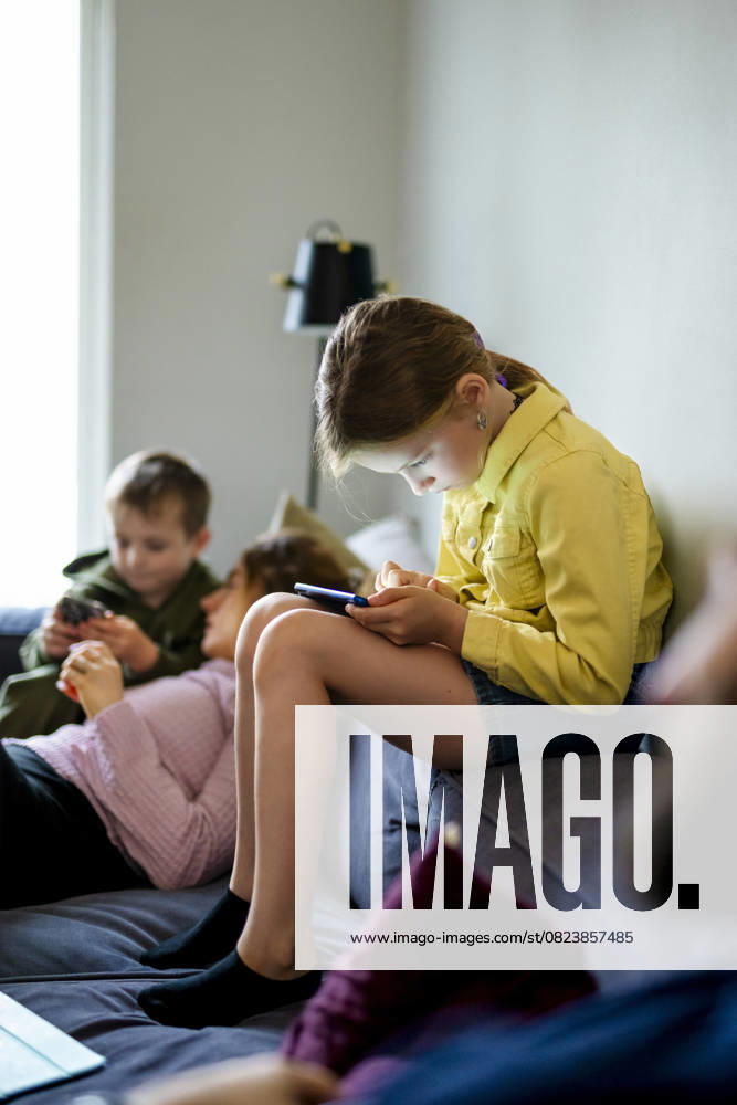 IMAGO Creative, Lifestyle, Gaming Full length of girl playing games on smart phone while sitting on sofa at home Sweden, Stockholm, model released, property released