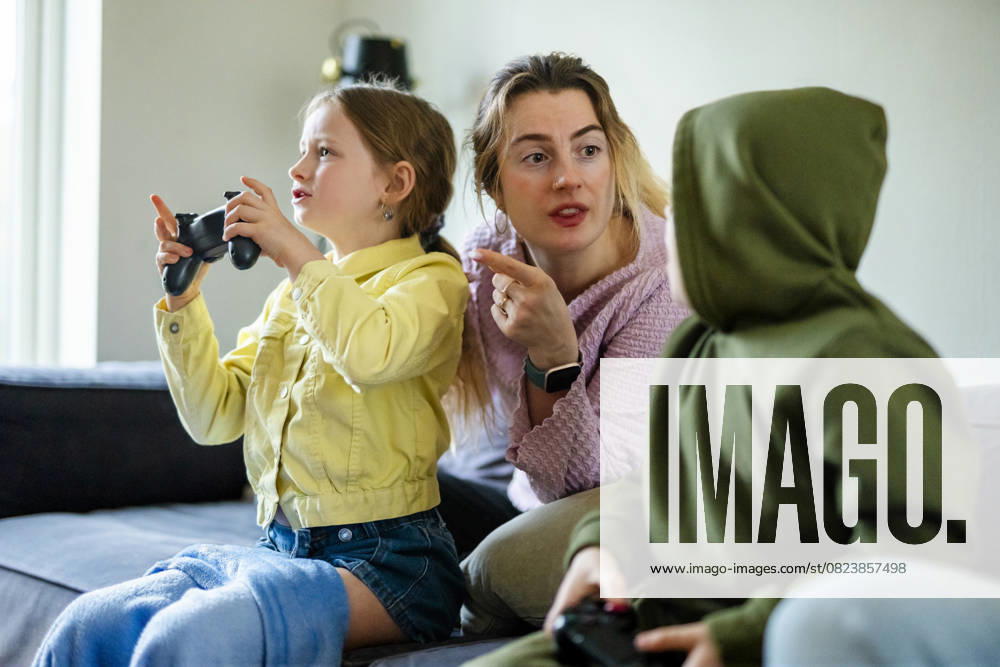 IMAGO Creative, Lifestyle, Gaming Mother talking with kids playing video games while sitting on sofa at home Sweden, Stockholm, model released, property released