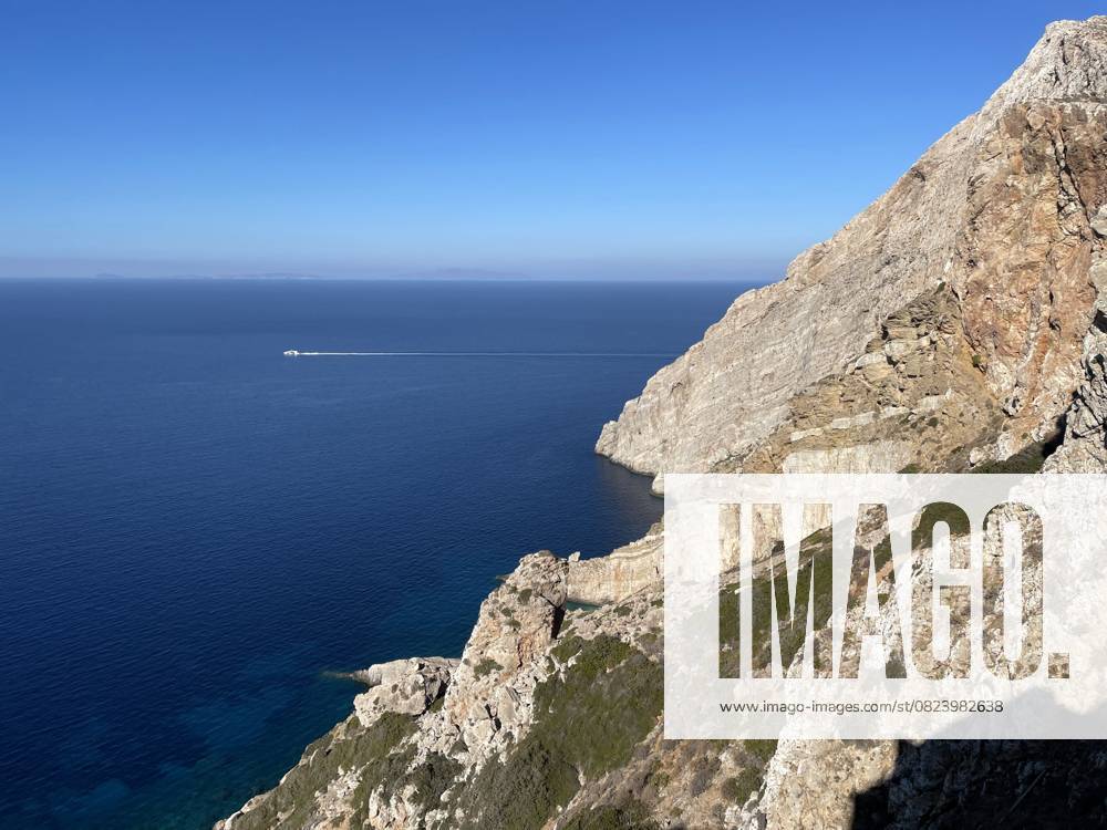 Tiefblaues Ägäisches Meer mit einer Klippe A cliff arises from the calm blue sea on the Aegean coast of the island of Folegandros. A boat is speeding off in the distance. (License=RF)