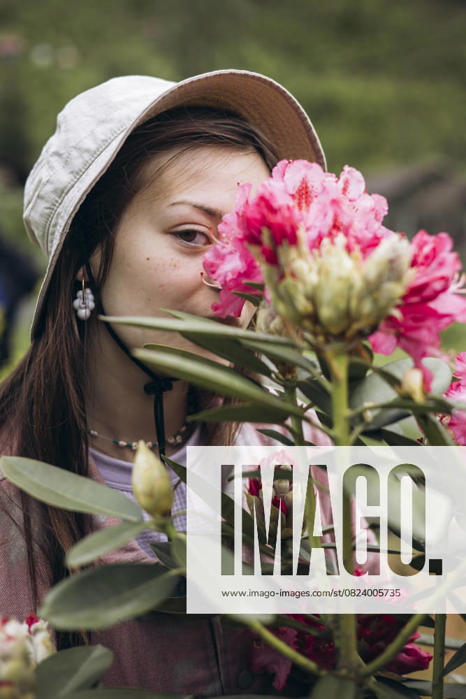 MR_ID29410_21441_OlhaHusonka.jpg A woman wearing a hat admires vibrant pink rhododendron flowers in a lush garden. The setting highlights a serene connection with nature and blooming beauty Model Released HannaYakimenko_ID29410_1000568_006