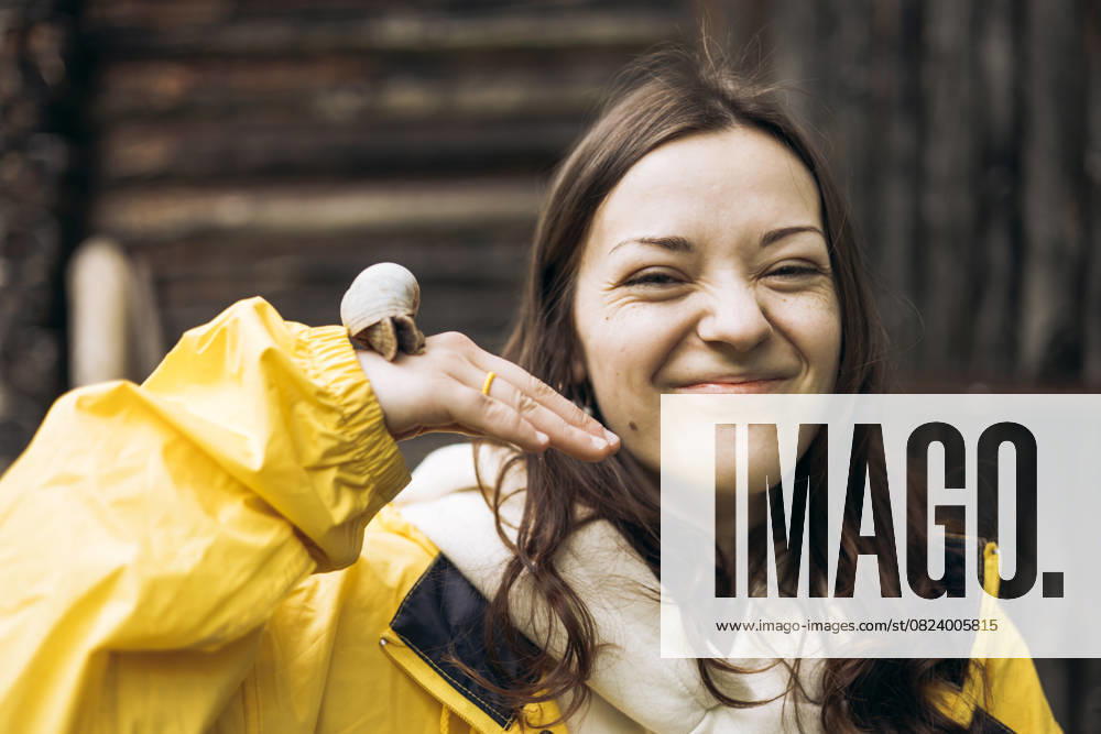 MR_ID29411_21442_OlhaHusonka.jpg, MR_ID29411_21444_MariaSavina.jpg, MR_ID29411_21443_VitaliiYakimenko.jpg A cheerful young woman in a yellow raincoat interacts naturally with a snail against a rustic backdrop in the mountains, embodying a spirit of adventure and joy Model Released HannaYakimenko_ID29411_1000754_013
