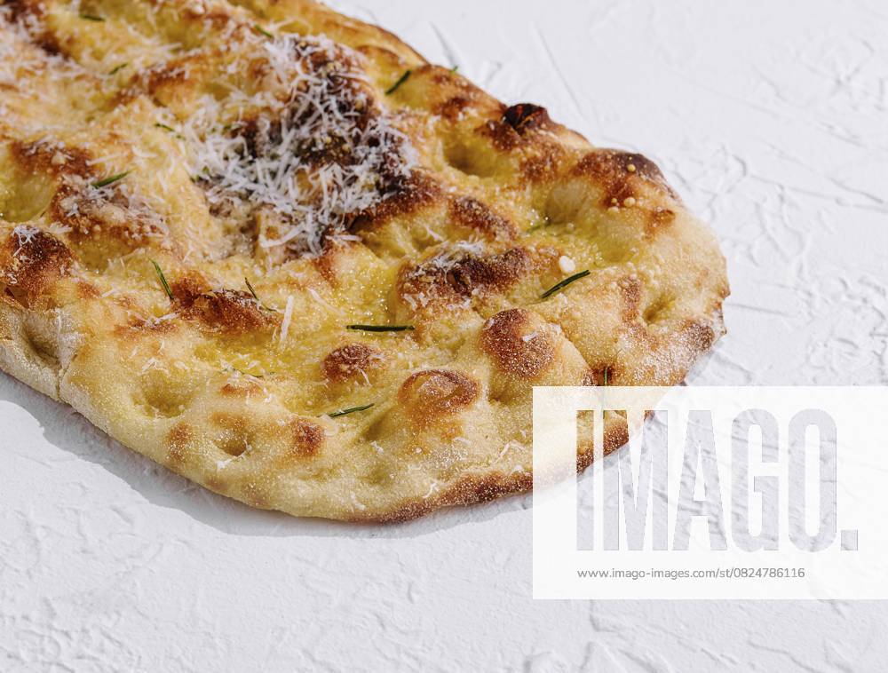 Foodfotografie, Handwerklich hergestelltes Fladenbrot mit geschmolzenem Käse und Kräutern, vor einer strukturierten weißen Oberfläche Food, Artisan flatbread with melted cheese and herbs, isolated on a textured white surface