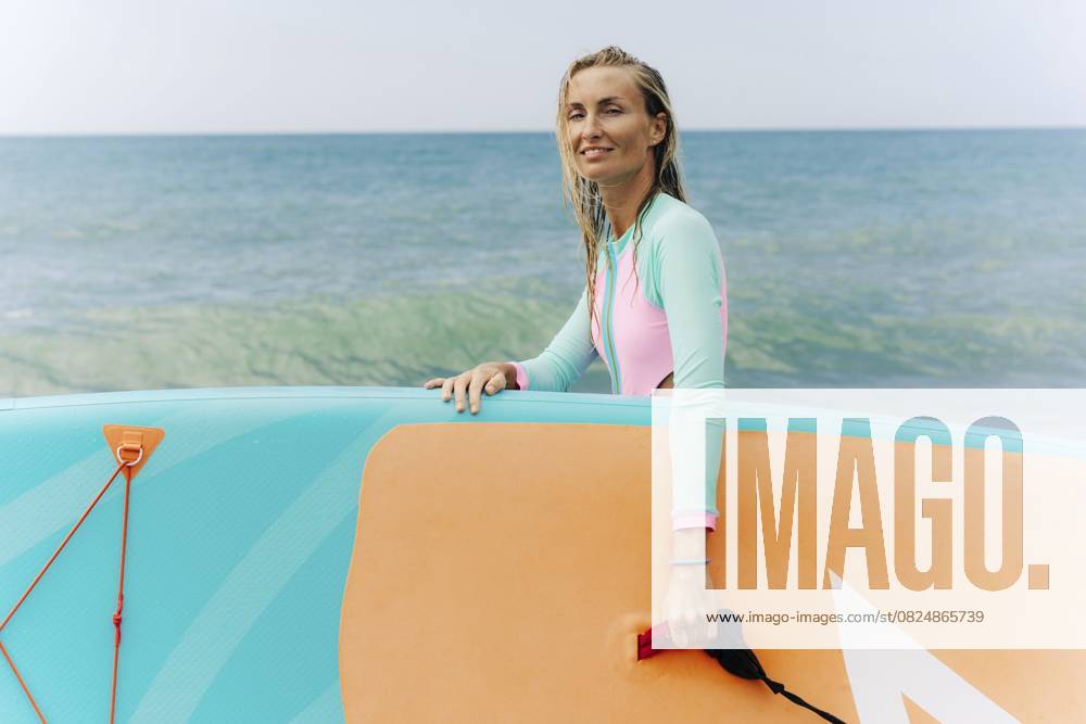 Junge sportliche blonde Frau steht am Strand und hält SUP surfen Young athletic blonde woman stands on the beach and holds SUP surf