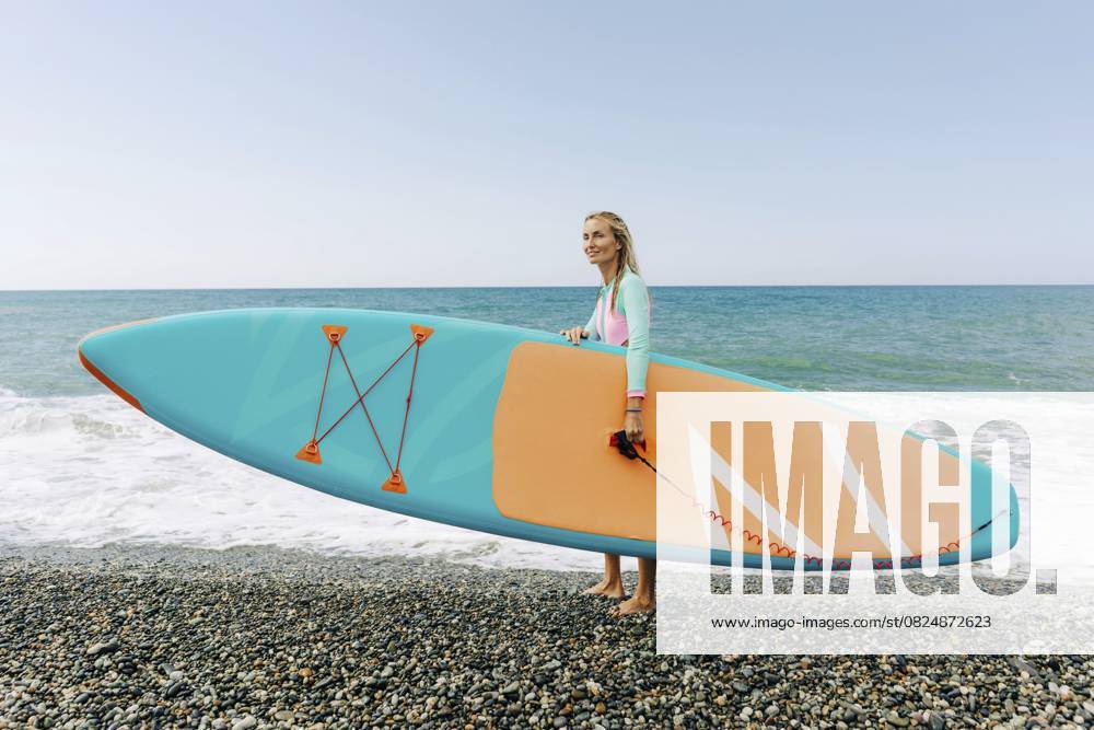 Junge sportliche blonde Frau steht am Strand und hält SUP surfen Young athletic blonde woman stands on the beach and holds SUP surf