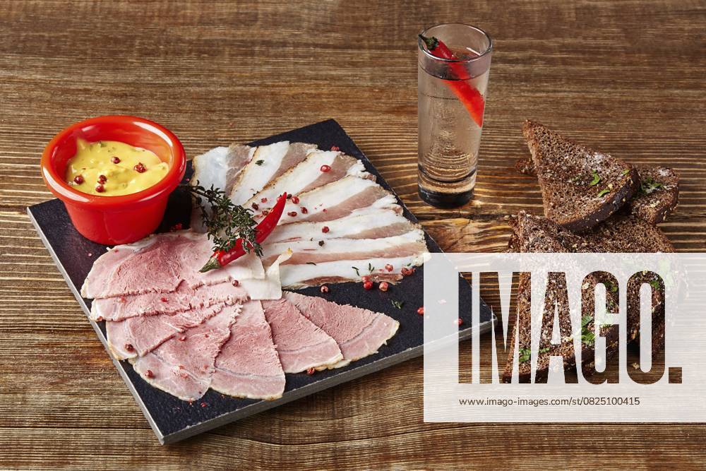 Aufgeschnittener Prosciutto oder Parmaschinken, Brot mit Salz, Senf und ein Glas Wodka mit würzigem Pfeffer auf einem Holztisch. Von oben gesehen. Konzept Restaurant Menü. Stillleben Sliced prosciutto or parma ham, bread with salt, mustard and a glass of vodka with spicy pepper on a wooden table. From top view. Concept restaurant menu. Still life