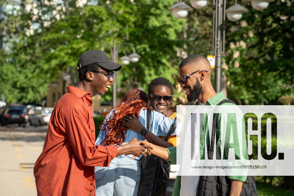 Fröhliche, fröhliche afroamerikanische Freunde, die ein plötzliches, angenehmes Treffen auf der Straße im Freien genießen Cheerful meeting of happy black friends. Women hugging cuddling, laughing loudly joyfully, men respectfully shake hands, smiling. African American people fellows students greeting say hello on street (License=RF) ,model released, Symbolfoto
