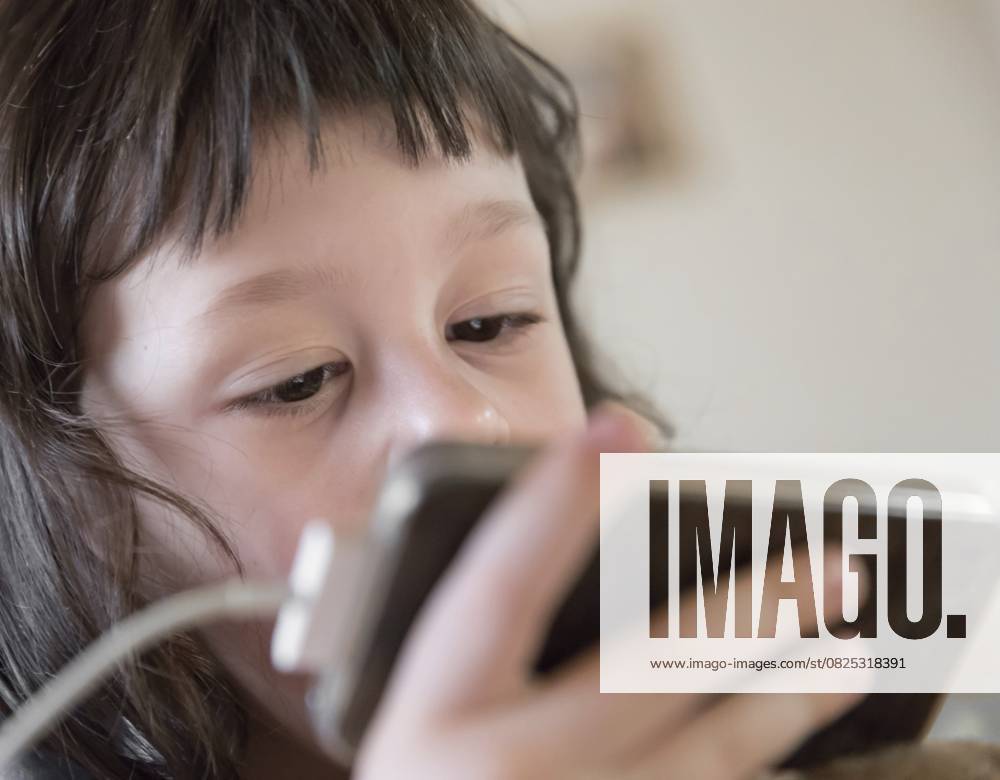 Niedliches kleines Kind, das den Bildschirm seines Smartphones genau beobachtet. Sucht nach digitalen Geräten, Kindheit und Bildung. Raum kopieren. Shallow dof Cute young child watching screen of smartphone closely. Digital device addiction, childhood and education. Copy space. Shallow dof