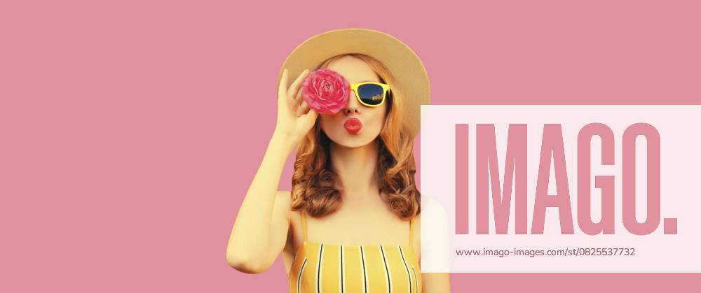 Sommer Porträt der stilvollen jungen Frau Modell bläst Kuss mit Blumenknospen auf der Suche nach etwas in runden Strohhut auf rosa Studio Hintergrund Summer portrait of stylish young woman model blowing kiss with flower buds looking for something in round straw hat on pink studio background