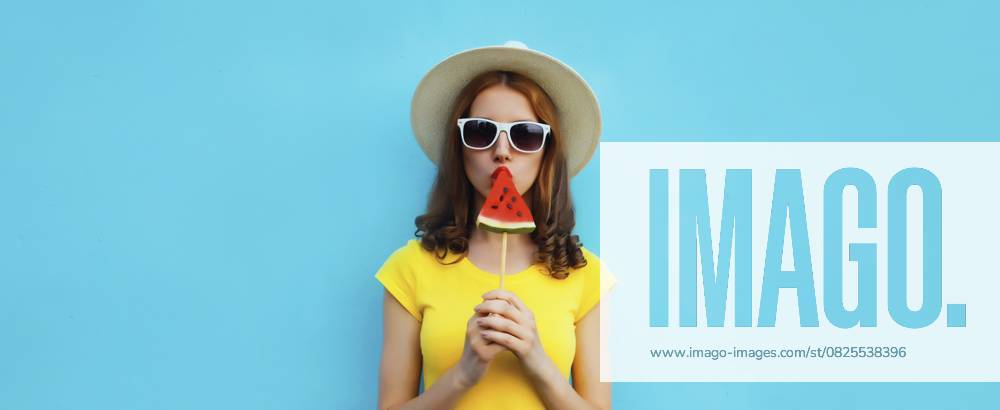 Sommer Porträt der stilvollen jungen Frau mit süßen saftigen Lutscher oder Eis geformt Scheibe Wassermelone trägt Strohhut auf blauen Studio Hintergrund Summer portrait of stylish young woman with sweet juicy lollipop or ice cream shaped slice of watermelon wearing straw hat on blue studio background
