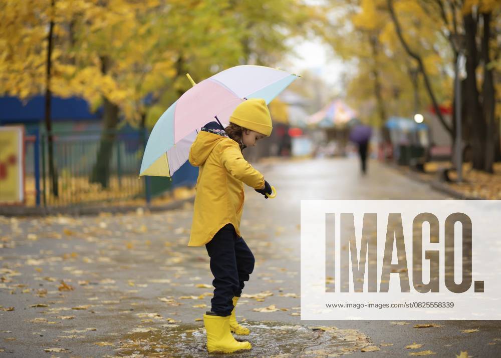Kind in gelben Gummistiefeln und Regenmantel steht auf Pfütze. Viel Spaß im Freien in der Herbstzeit. Kinder Aktivität Child in yellow rubber boots and raincoat standing on puddle. Have fun outdoors in autumn season. Children activity