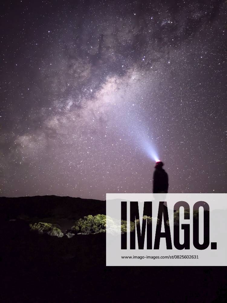 Eine Person steht mit einer Stirnlampe unter einem Sternenhimmel und beobachtet die Milchstraße, La Réunion, Frankreich, Afrika A person stands stargazing with a headlamp under a starry sky and the Milky Way, La Réunion, France, Africa