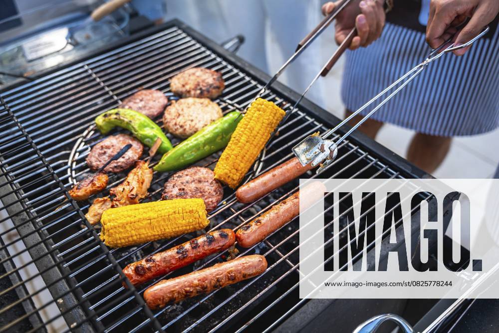 Köche grillen mehrere Hot Dogs, Hamburger, Mais und Paprika auf einem heißen Grill für eine sommerliche Grillparty Chefs grilling several hot dogs, hamburgers, corn and peppers on a hot grill for a summer barbecue party