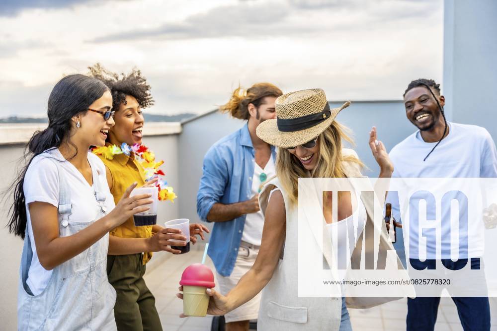 Fröhliche multiethnische Freunde genießen Cocktails und tanzen fröhlich auf einer lebhaften Dachparty vor der atemberaubenden Skyline der Stadt Cheerful multi ethnic friends enjoying cocktails and dancing joyfully at a vibrant rooftop party against a stunning city skyline