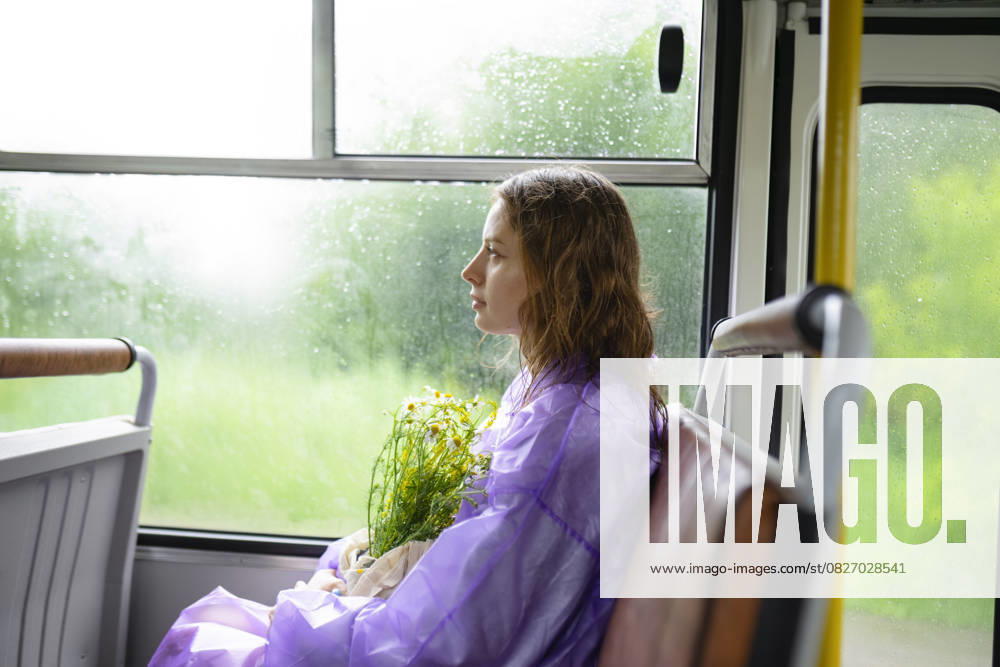 IMAGO Creative, Jahreszeit Sommer, Regen, Sommerregen Creative Highlight Symbolbilder Woman in purple raincoat holding wild flowers sitting on a bus model released, Symbolfoto, VCF00804