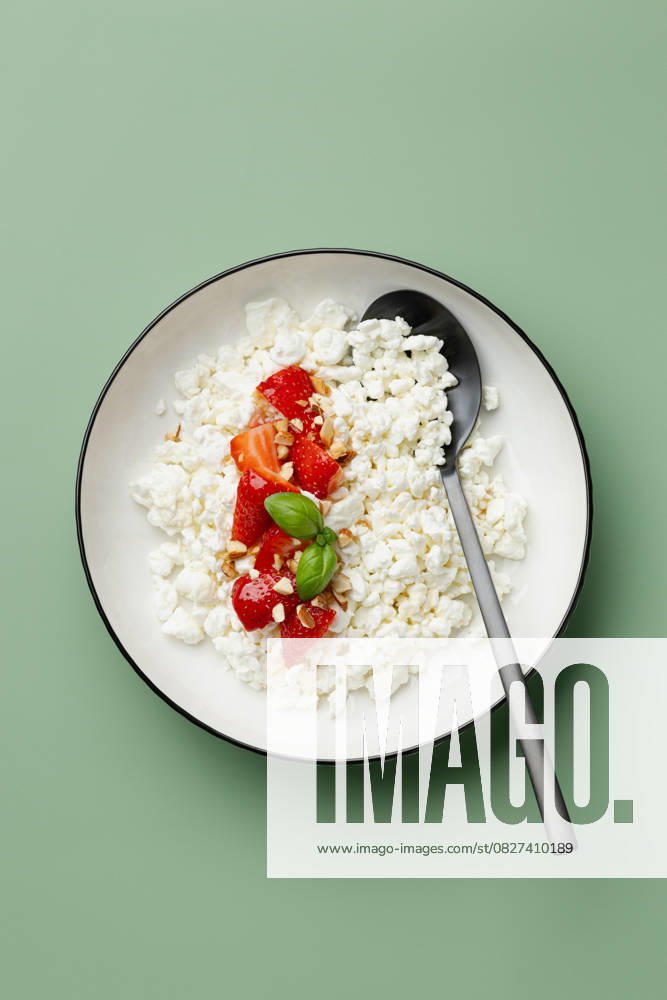 IMAGO Creative, Food, High Protein Frühstück Cottage cheese and fresh strawberries in a bowl A delightful bowl of creamy cottage cheese topped with fresh, juicy strawberries and a sprig of basil. Perfect for a healthy breakfast or snack on a pastel green background Model Released JuliaKuvaldina_ID30036_1014110_006
