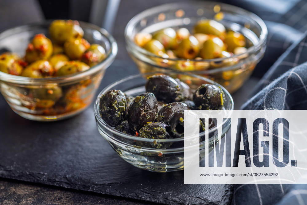 Tapas. Aromatisierte eingelegte Oliven in einer Schale auf einem schwarzen Tisch. Tapas. Flavored pickled olives in bowl on a black table. (License=RF)