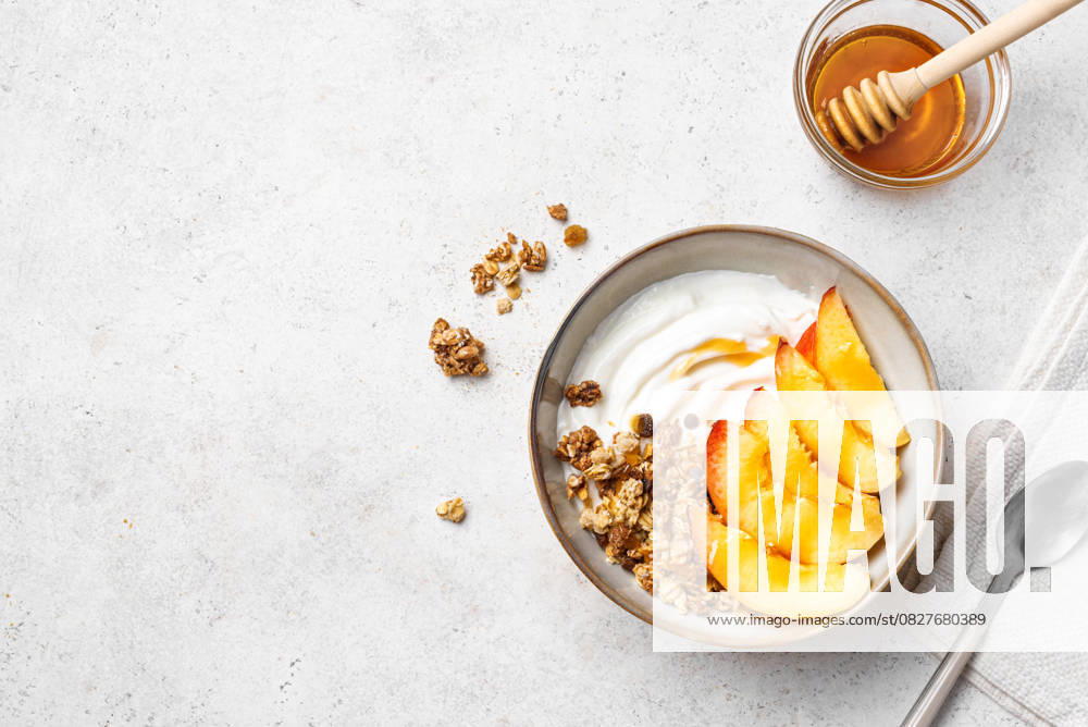 Müslischale mit griechischem Joghurt, Pfirsich und Honig Granola bowl for healthy breakfast. Homemade granola with greek yogurt, peaches and honey on white background, top view, copy space. Healthy eating, seasonal summer breakfast template. (License=RF)