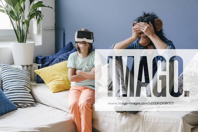 Father wearing monkey mask sitting next to son wearing VR glasses at home model released Symbolfoto property released KNSF03648