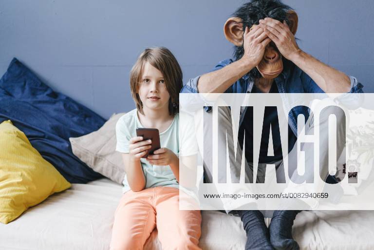 Father wearing monkey mask sitting next to son using smartphone at home model released Symbolfoto property released KNSF03649