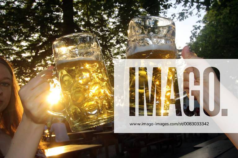Two measure mugs of beer in the evening sun of a warm spring day in the beer garden. Royal deer garden in Munich. Bavaria. Germany