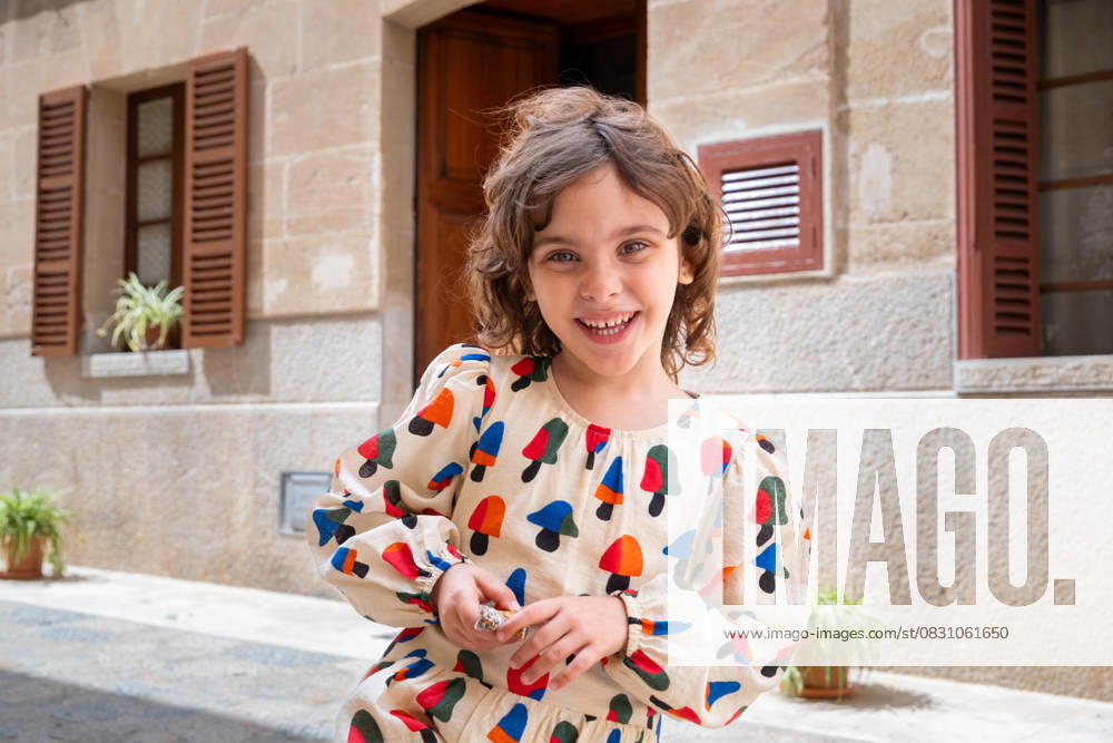 MR_ID30398_21876_MariaAntoniaVanrell.jpg, MR_ID30398_21874_MargotBordoy.jpg, MR_ID30398_21875_GinaBordoy.jpg A joyful child, dressed in colorful attire, plays in the sunlit street of a quaint village, expressing happiness and innocence amidst charming rustic surroundings Model Released Dbordoy_ID30398_1025542_001