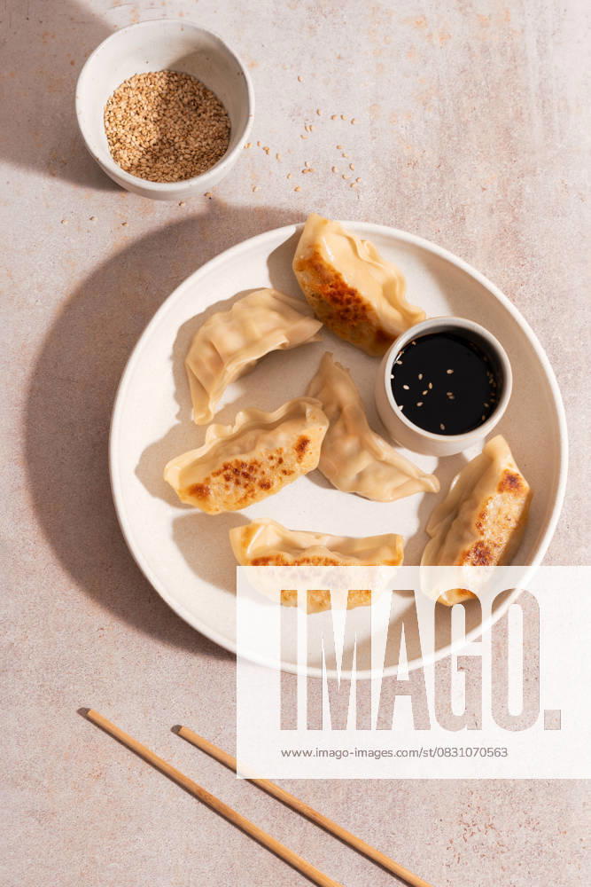 IMAGO Creative, Food, Dumplings Top view of chicken vegetable gyozas on white plate Top view of golden-brown chicken and vegetable gyozas served on a white plate with a small bowl of soy sauce. Background features light stone surface and chopsticks. Model Released MaiderAlvarez_ID30883_1046944_003