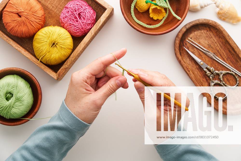 Top view of a woman crocheting in her artisan studio Top view of cropped unrecognizable hands of a woman crocheting in her studio. Surrounded by colorful yarn and crochet tools, she crafts intricate handmade designs. Model Released Natanordic_ID30668_1037815_002
