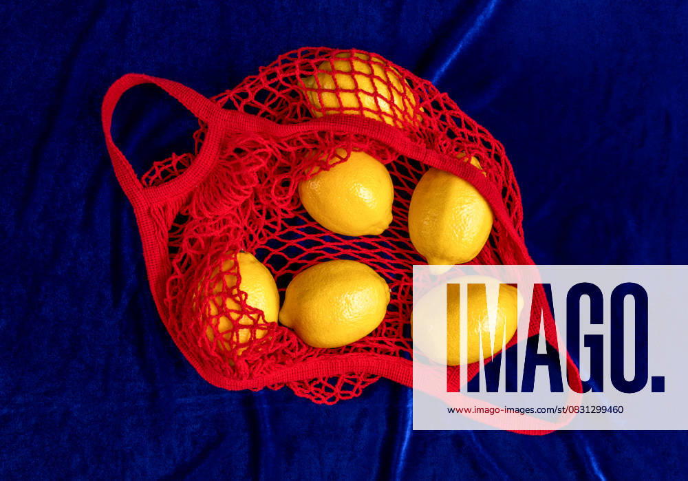 Fresh lemons in red string bag on blue velvet still life, AAF00119