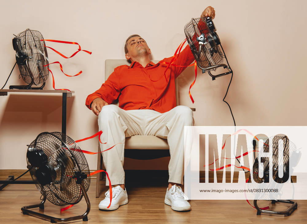 Mid adult sitting in armchair cooling down with fans during extreme heat model released, Symbolfoto, AAF00130