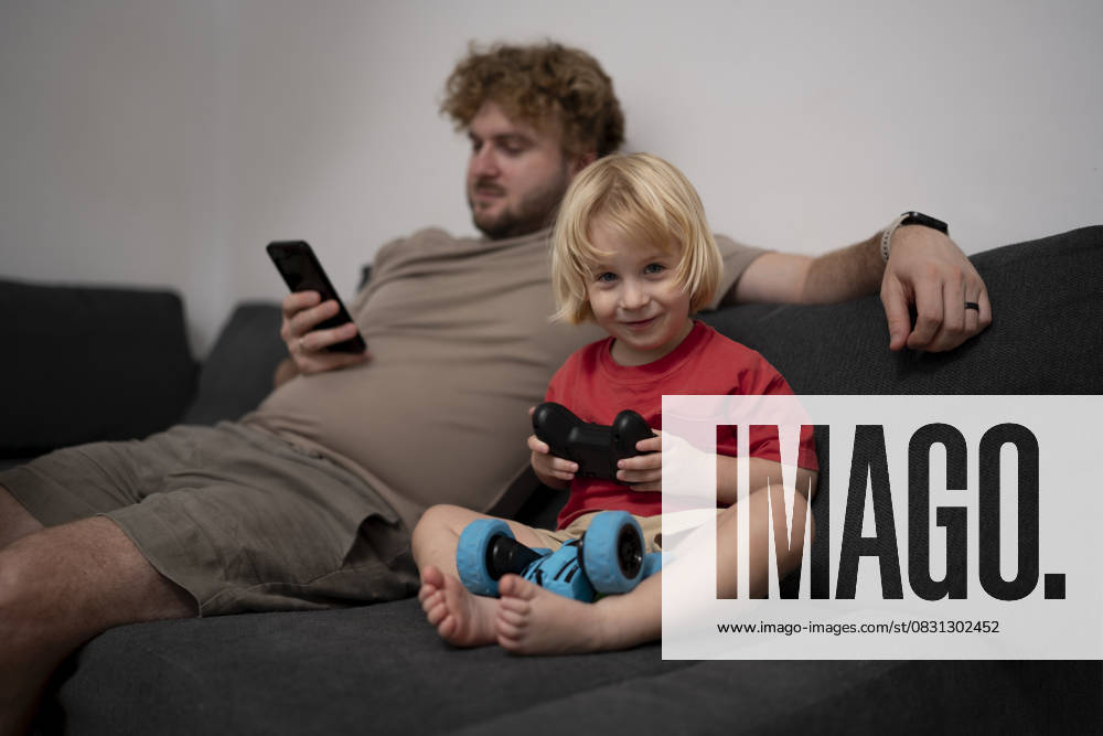 IMAGO Creative, Lifestyle, Gaming Father and son relaxing at home playing video game on sofa model released, Symbolfoto property released, OGSF00215