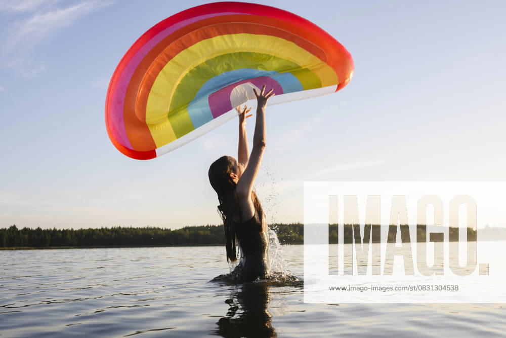 Person in swim suit playing with rainbow float in lake during summer model released, Symbolfoto, EYAF03494