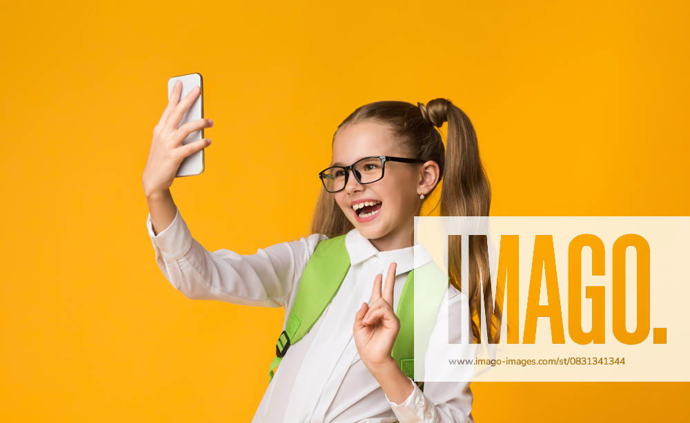 Schoolgirl Using Smartphone Taking Selfie Gesturing V-Sign, Yellow Background School Selfie. Happy Schoolgirl Using Smartphone Taking Self-Portrait Gesturing Victory Sign On Yellow Studio Background. Copy Space, model released, , 60918330.jpg RECORD DATE NOT STATED