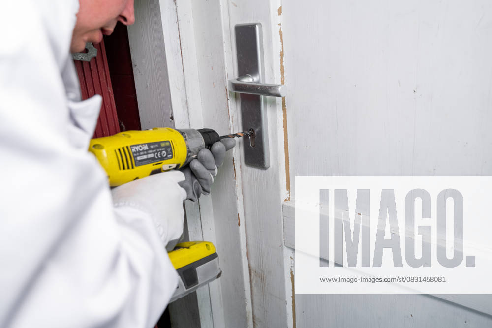 A mechanic opens a front door with a drill. Symbolic image for locksmith services, door openings in the event of lost keys