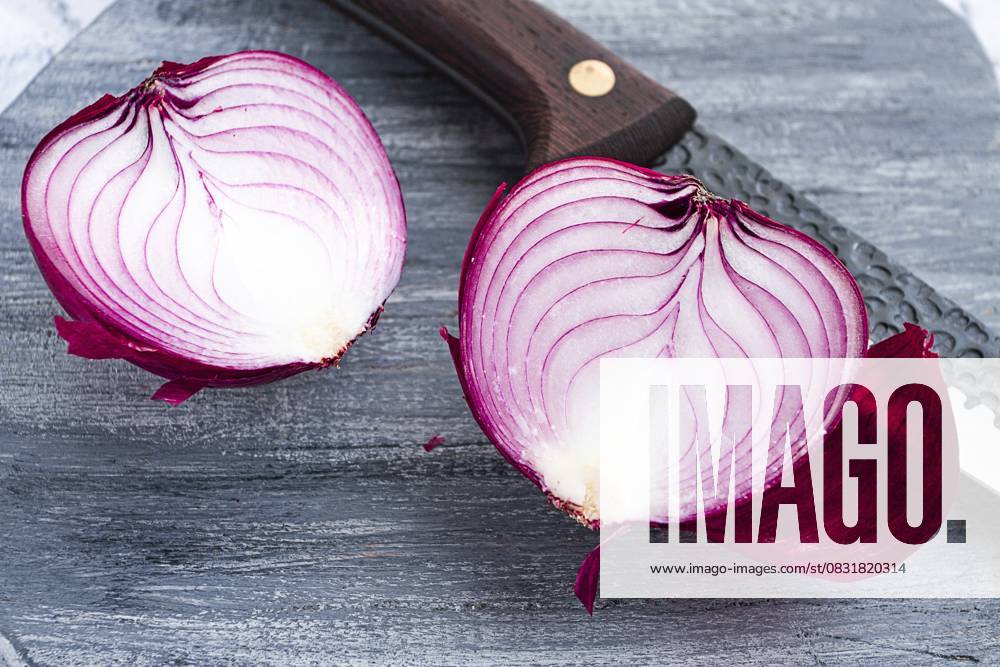 Eine leuchtend rote Zwiebel wird auf einem rustikalen Holzbrett neben einem scharfen Messer in zwei Hälften geschnitten, bereit zum Kochen A vibrant red onion is cut in half, on a rustic wooden chopping board beside a sharp knife, ready for cooking
