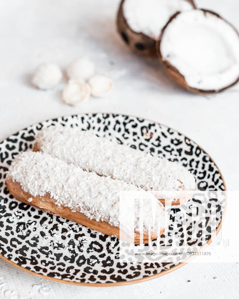 Eclairs with Shredded Coconut on Leopard Print Plate and Coconuts Two eclairs topped with shredded coconut rest on a leopard print plate, surrounded by halved coconuts and white confections on a white table., 64438240.jpg RECORD DATE NOT STATED