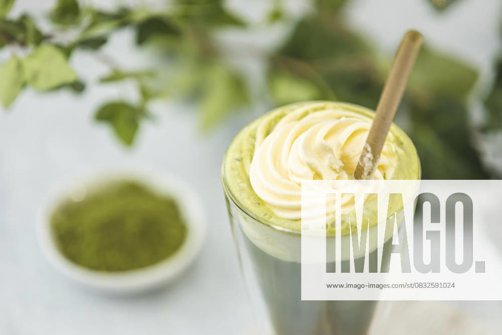 Matcha latte with whipped cream and powdered tea in a glass Glass of matcha latte topped with whipped cream and accompanied by powdered green tea on a blurred background with green leaves, 94703966.jpg RECORD DATE NOT STATED