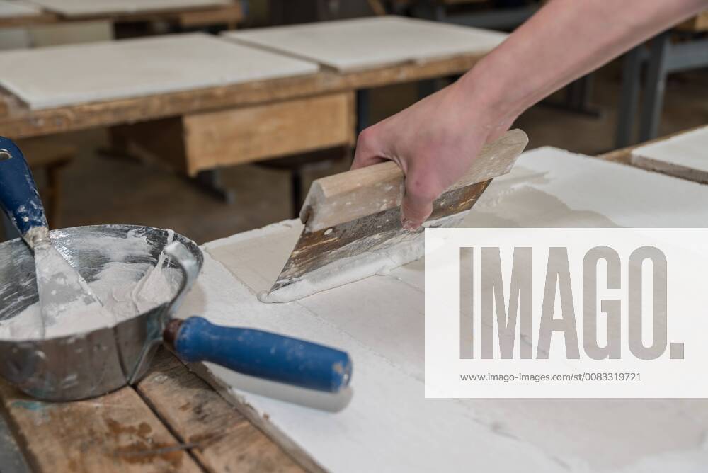 Bricklayer applies putty paint with a broad spatula Construction worker applying putty with a wide spatula 1077403795