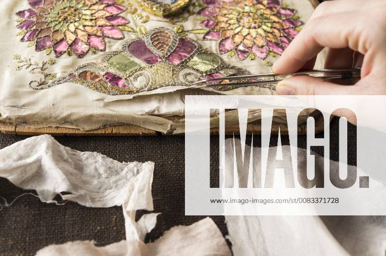 Restaurationatelier Restauratorin Hand inspects artfully embroidered silk scarf torn with tweezers Munich Bavaria Germany Europe